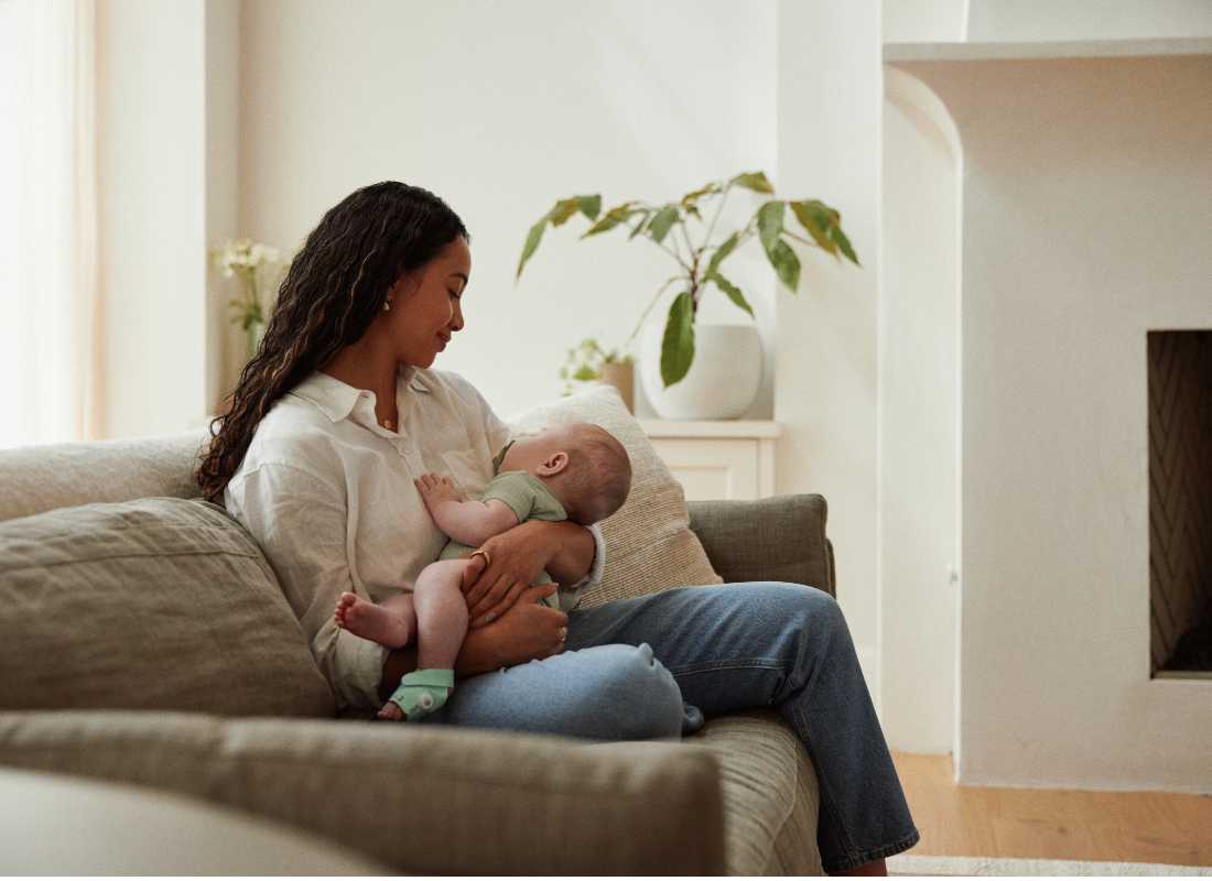 Mum sitting on sofa holding sleeping baby
