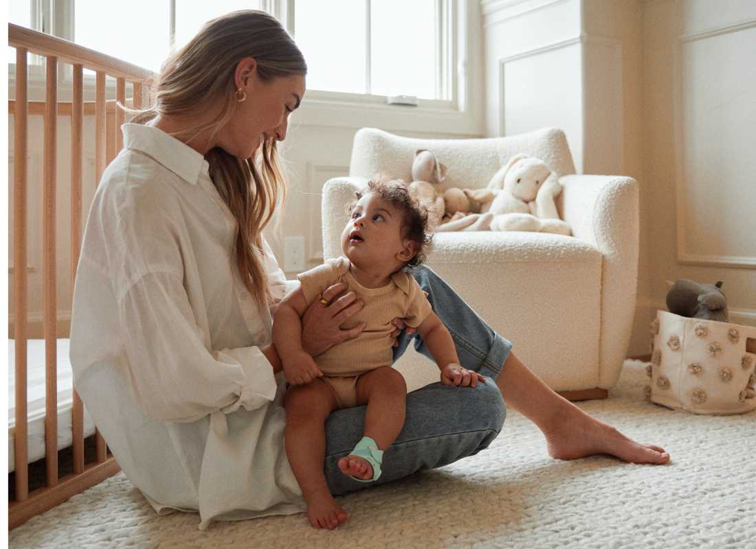 Mum sitting on the floor, next to a cot with a baby in her lap