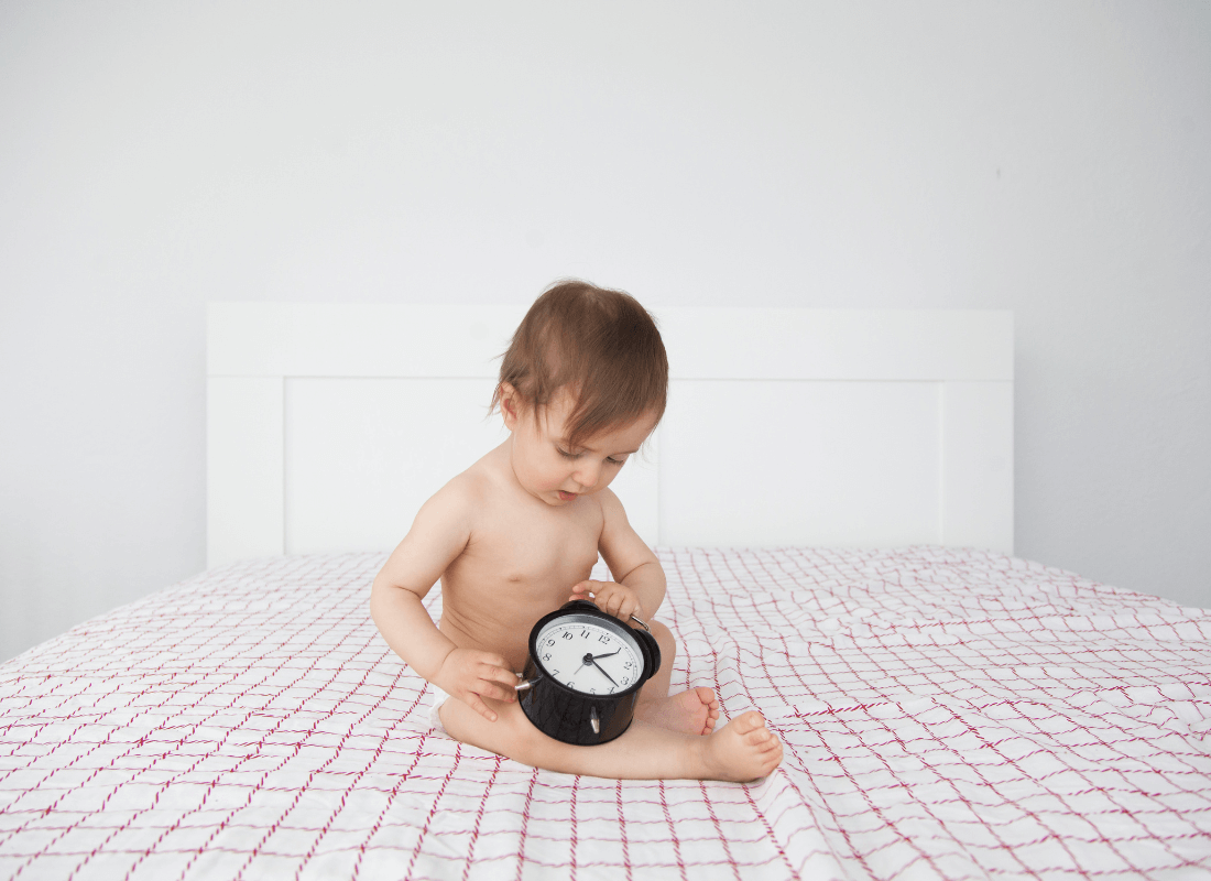 Baby sat on bed holding a clock