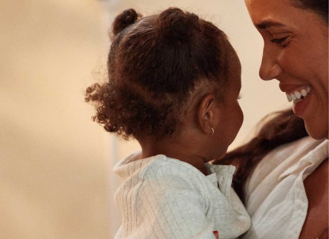 Women hold's a baby and is smiling at them.