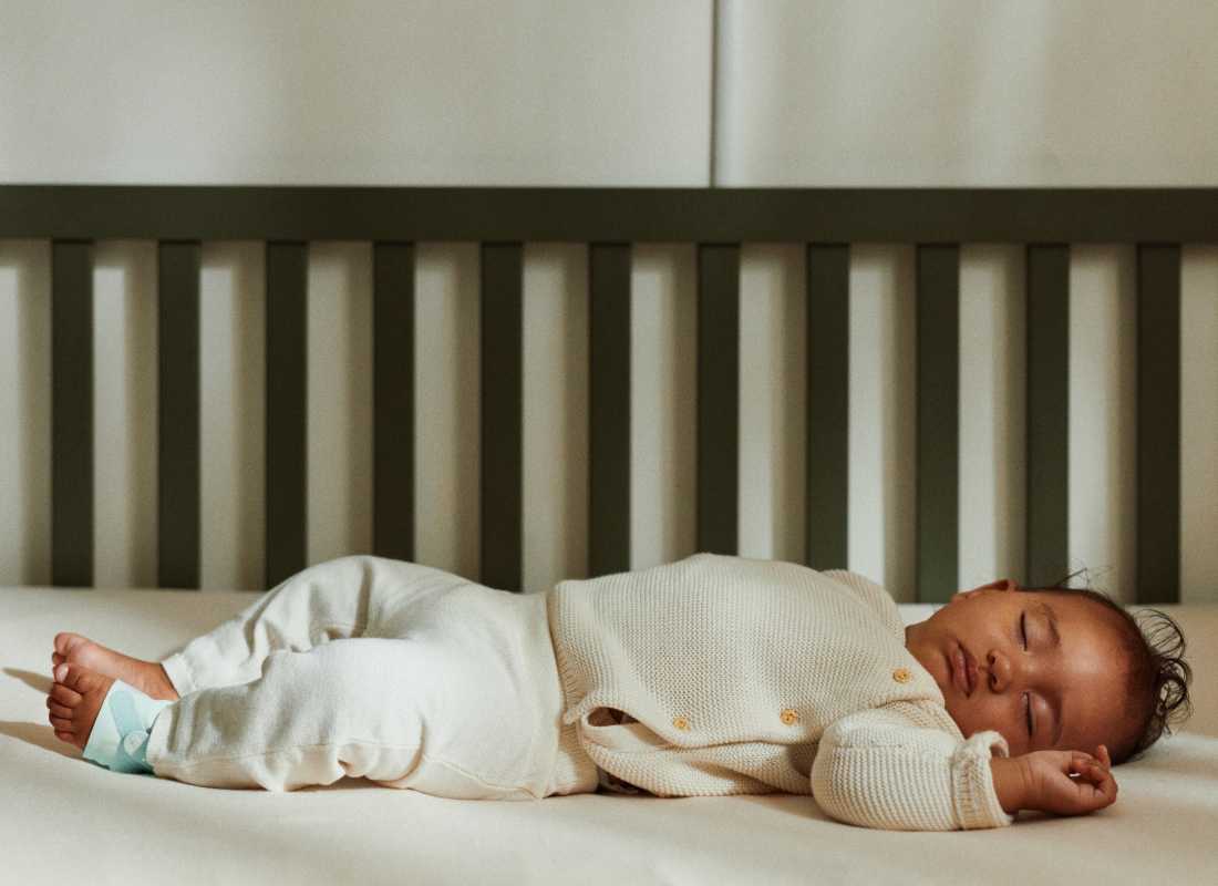 Baby asleep in a cot with an Owlet mint Dream Sock on