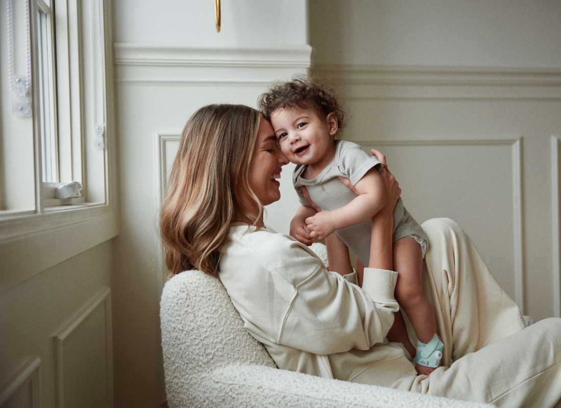 Mum holds baby Wearing a Mint Owlet Dream Sock, up to her forehead,