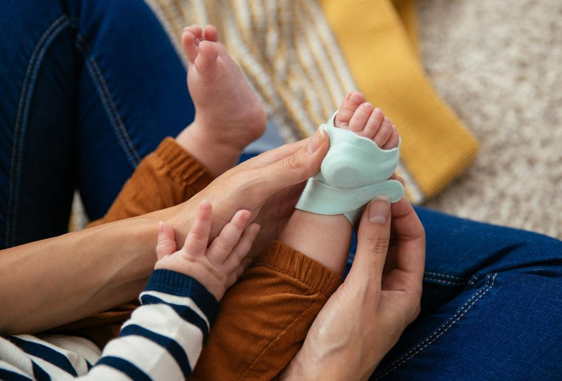 Hands putting an Owlet Smart Sock on baby foot